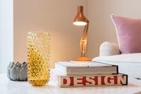 Detail of glassware and books on living room table with lamp in background 