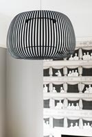 Black and white stripy lampshade on pendant light with patterned wallpaper behind 