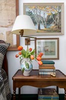 Lamp and vase of tulips on wooden bedside table in country bedroom 