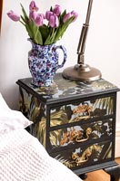 Decoratively painted bedside cabinet with vintage jug full of pink tulips 