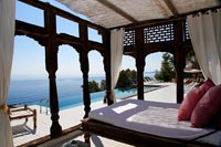 Decorative pergola with large bed on outdoor terrace with pool and sea views 