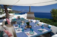 Large tiled outdoor dining table under canopy with coastal views 