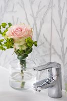 Rose in glass next to bathroom tap on sink 