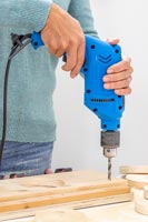 Woman using a drill to make small holes in the corners of the boards to enable hanging