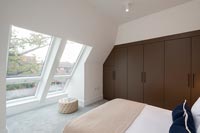 Modern bedroom with pitched roof windows and brown built-in wardrobe 
