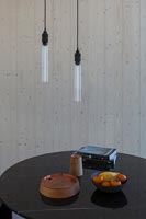 Small circular table and bare pendant lighting next to wooden wall 