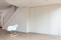 Minimal white hallway with built-in under stair cupboards and single chair