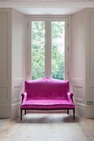 Bright pink antique sofa next to window