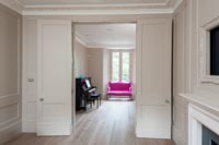 View through double doors into music room with bright pink sofa at one end 