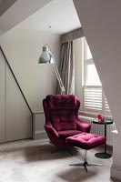 Red velvet armchair and foot stool next to window with large silver floor lamp 