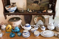 Crockery on wooden sideboard with shelf of ornaments above 