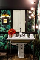 Eclectic bathroom with tropical wallpaper and lit up mirror above sink 