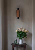 Flower arrangement on small table under modern wall light 