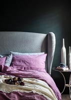Pink bedding in modern bedroom with grey headboard and black painted walls 