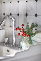 Pine tree foliage and red berries in glass jar next to sink 