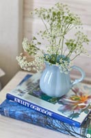 Pale blue jug of cut wild flowers on bedside table with books 