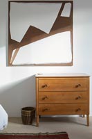Wooden chest of drawers and modern artwork in bedroom 