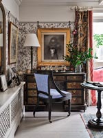 Antique desk in corner of classic living room with patterned wallpaper 