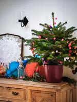 Small Christmas tree decorated with colourful pompoms on wooden sideboard 