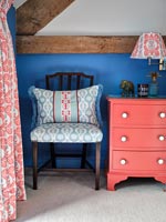 Pink painted bedside cabinet against blue painted wall in country bedroom