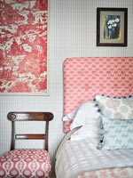 Patterned fabric headboard and chair cover in country bedroom 