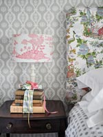 Stack of books on bedside table with clashing patterned headboard and lamp