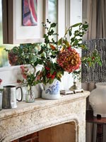 Flower and foliage arrangement in jug on mantelpiece 