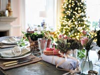 Christmas gifts on dining table with tree in background 