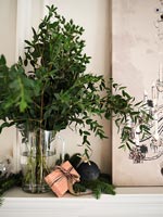 Evergreen foliage in vase on mantelpiece with Christmas gifts 