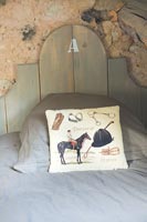 Equestrian themed cushion on bed with exposed stone wall behind 