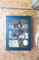 Display cabinet filled with ornaments mounted on exposed stone wall 