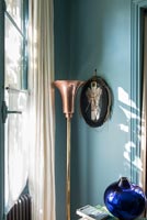 Decorative copper floor lamp and fabric picture on blue painted wall