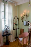 Green painted wall and pink antique chair surrounded by ornaments 