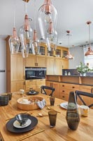 Modern wooden kitchen diner with rose coloured light fittings  