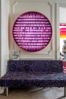 Purple patterned sofa under colourful artwork 