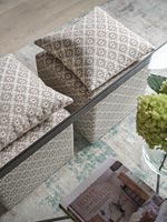 Patterned cushions and matching footstools next to glass table 