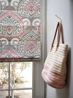 Bag on wall next to patterned pink and grey blinds over window 