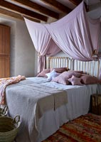 Country bedroom with pink fabric canopy hanging from wooden beams 