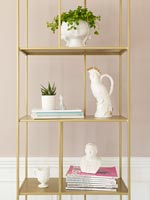 House plants and white ornaments on gold shelving 