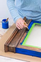 Woman painting old wooden frame with blue paint - memories notice board 