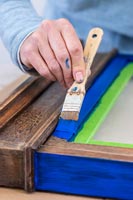 Woman painting old wooden frame with blue paint - memories notice board 