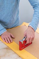 Woman stapling fabric to cork board - memories notice board craft project 
