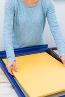 Woman placing fabric covered cork board into newly painted frame 