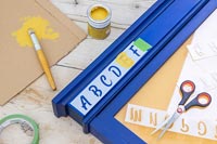 Letter stencils - painting onto blue wooden frame of notice board 