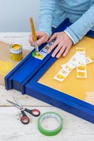 Adding stencil lettering to blue painted notice board frame 