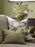 Floral cushion on sofa with flowers in vase behind 