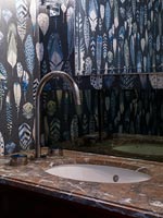 Patterned wallpaper and marble top around bathroom sink 