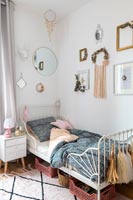 Metal framed daybed in childrens bedroom with wall display of small mirrors 