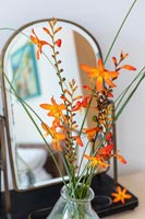 Detail of orange flowers in vase on dressing table by mirror 
