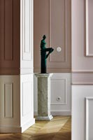 Small green sculpture of a woman on marble plinth in hallway 